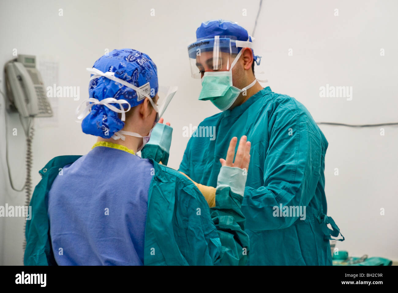 Eine Frau Chirurg wird in einem sterilen Kleid von ihr Peeling-Techniker unterstützt, vor dem Ausführen eines Vorgangs Stockfoto