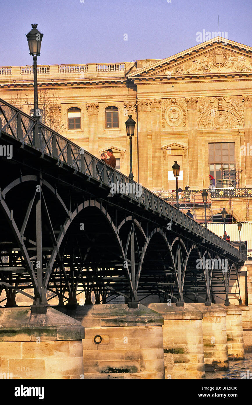 LIEBHABER, EIN PAAR UMARMT, PONT DES ARTS MIT DEM LOUVRE IM HINTERGRUND, PARIS 6. ARRONDISSEMENT, PARIS (75), FRANKREICH Stockfoto