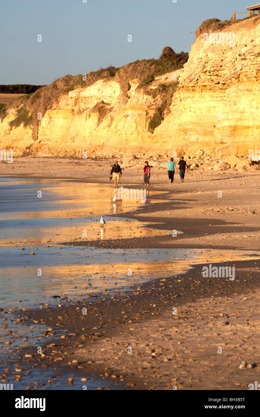 Menschen, die in der späten Nachmittagssonne bei Flut am Strand entlang spazieren. Stockfoto