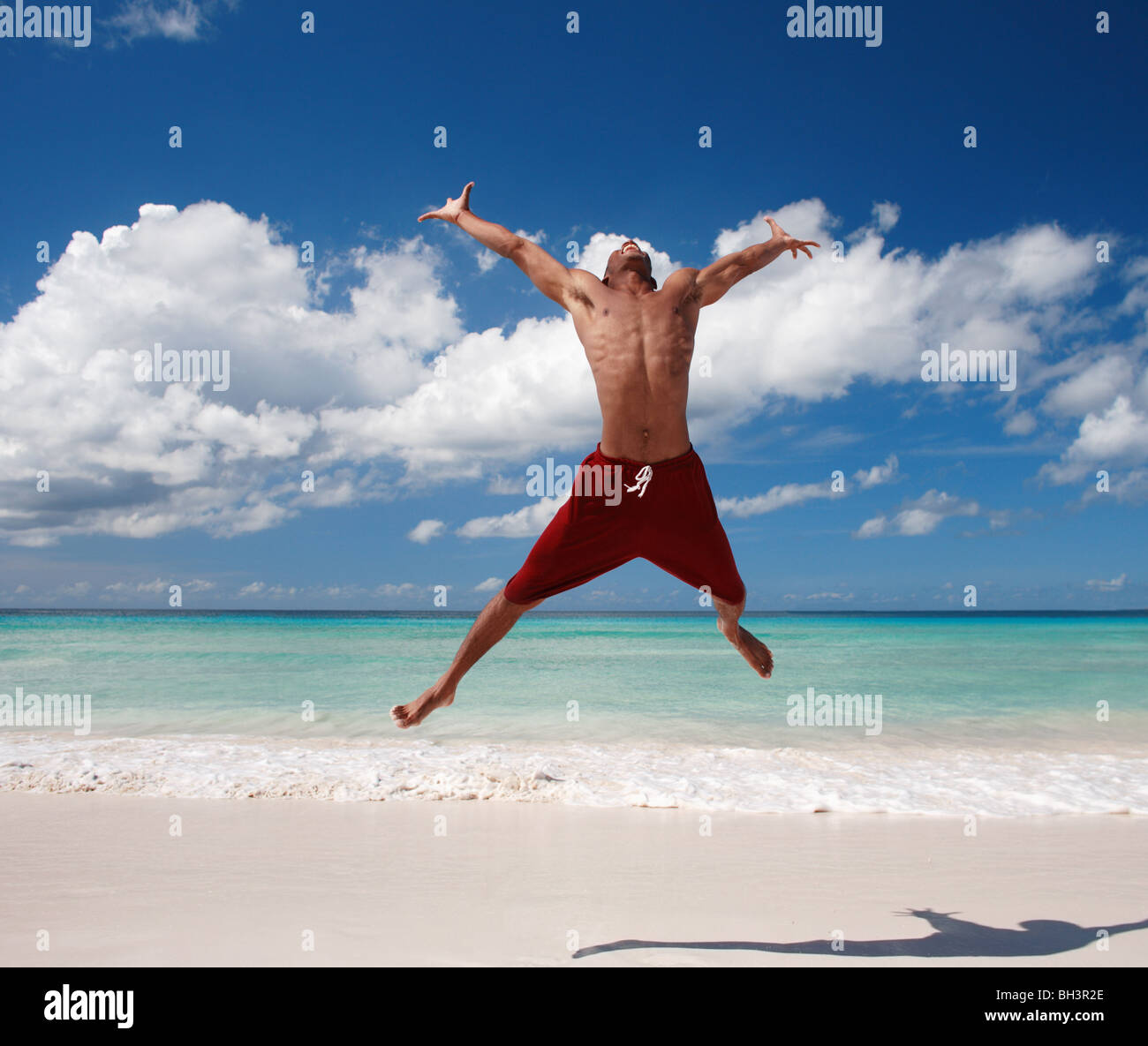 Junger Mann springt auf einem tropischen Strand, Lächeln Stockfoto