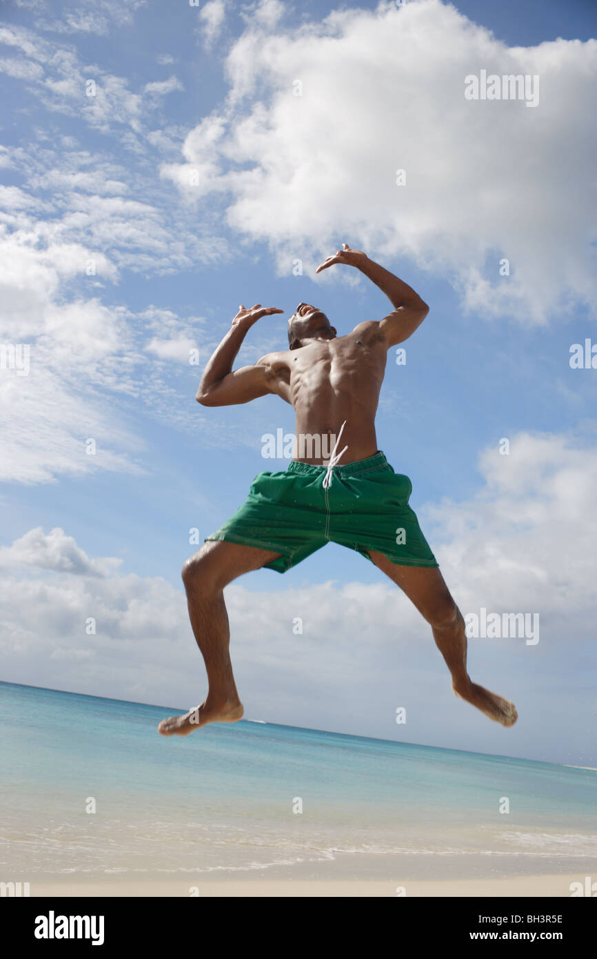 Junger Mann springt auf einem tropischen Strand, Lächeln Stockfoto
