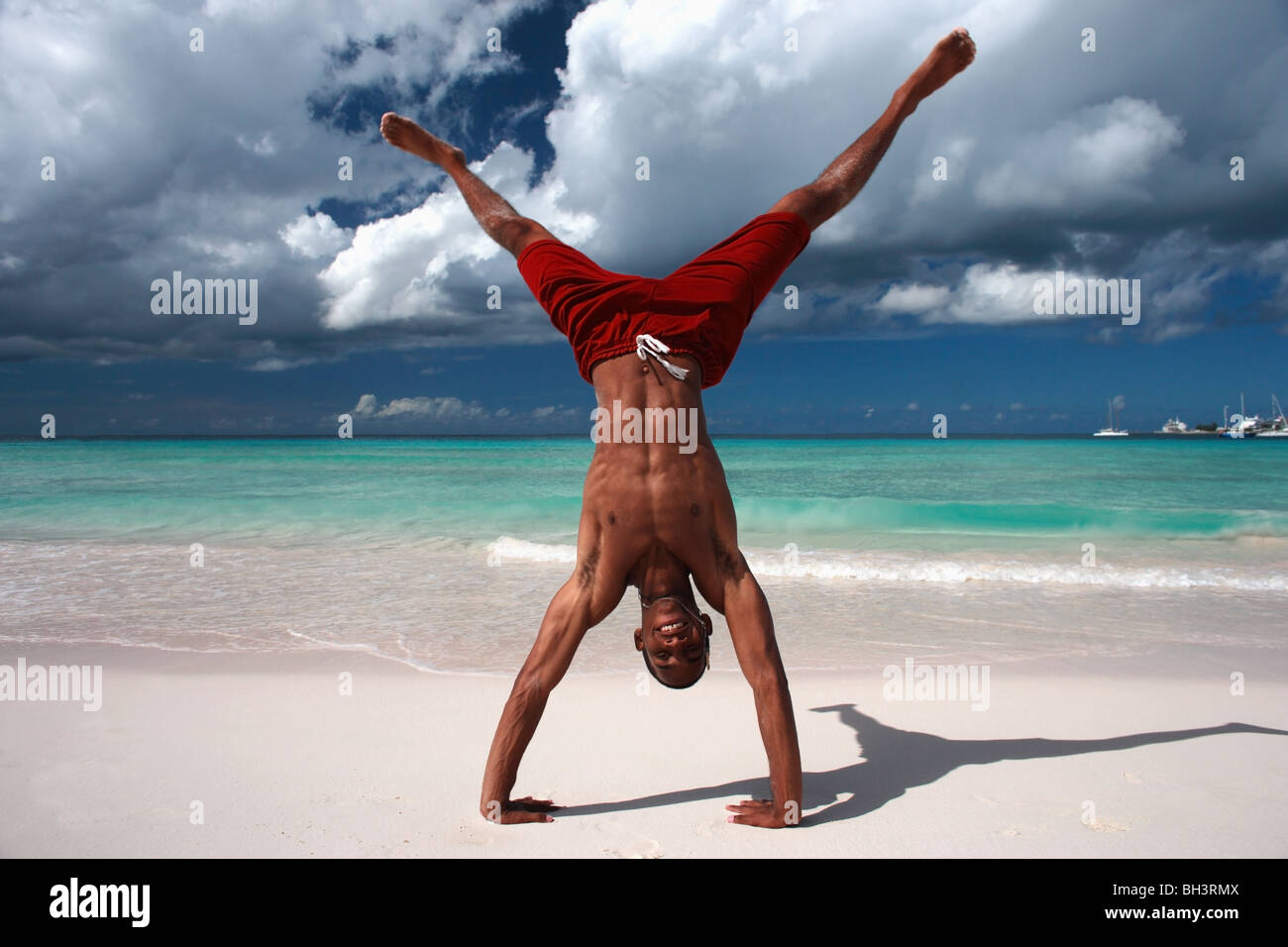 Junger Mann ausführen einen Handstand auf einem tropischen Strand, Lächeln Stockfoto