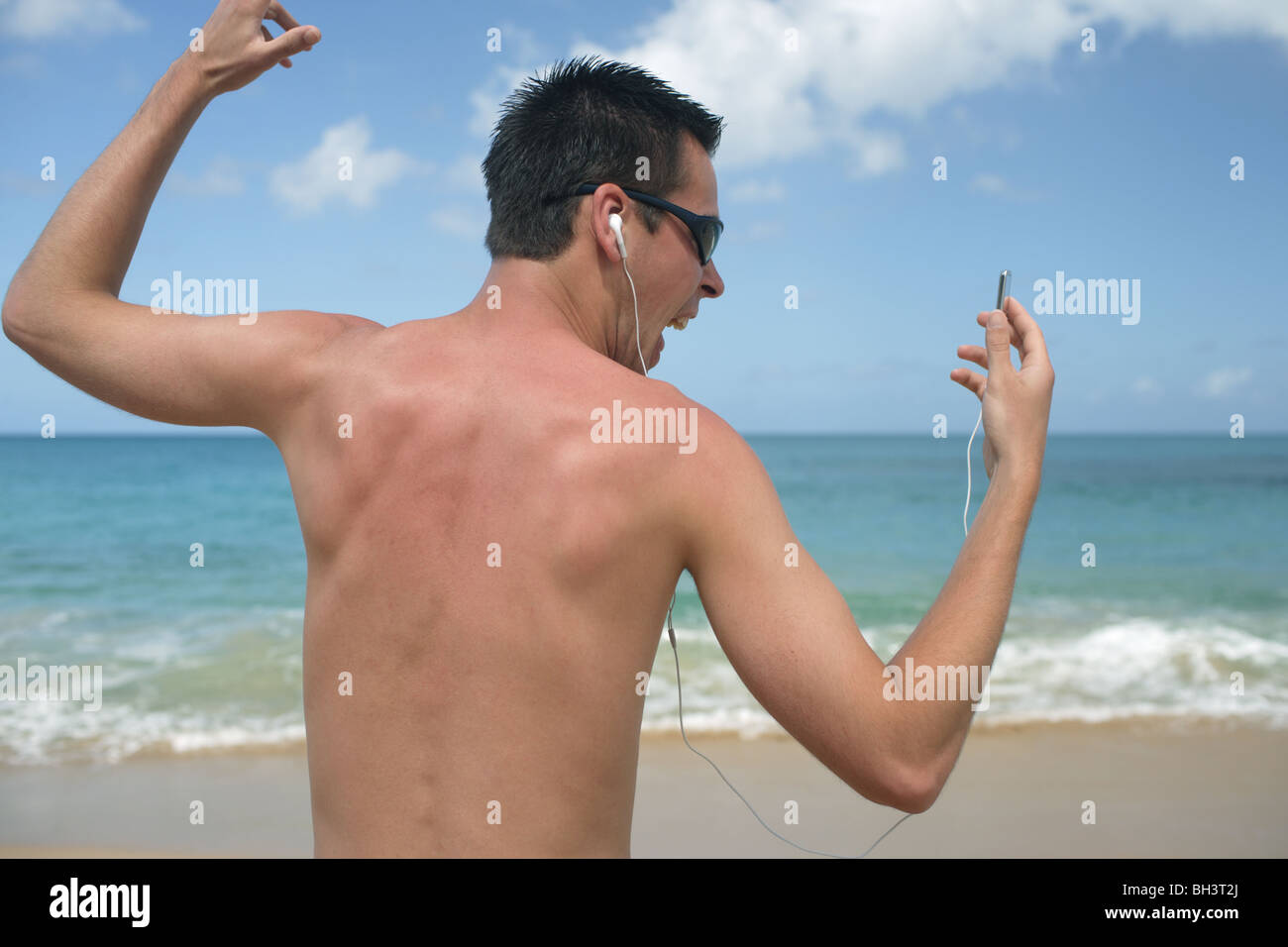 Junger Mann Musik auf einen MP3-Player hören und singen auf einem einsamen tropischen Strand Stockfoto