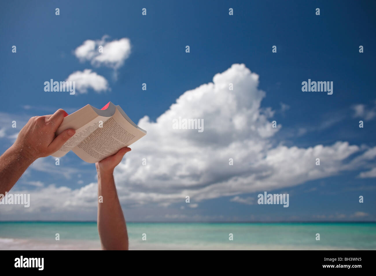 Ein Mann Hände halten eine offenen Papier zurück buchen in Richtung des Himmels an einem tropischen Strand Stockfoto