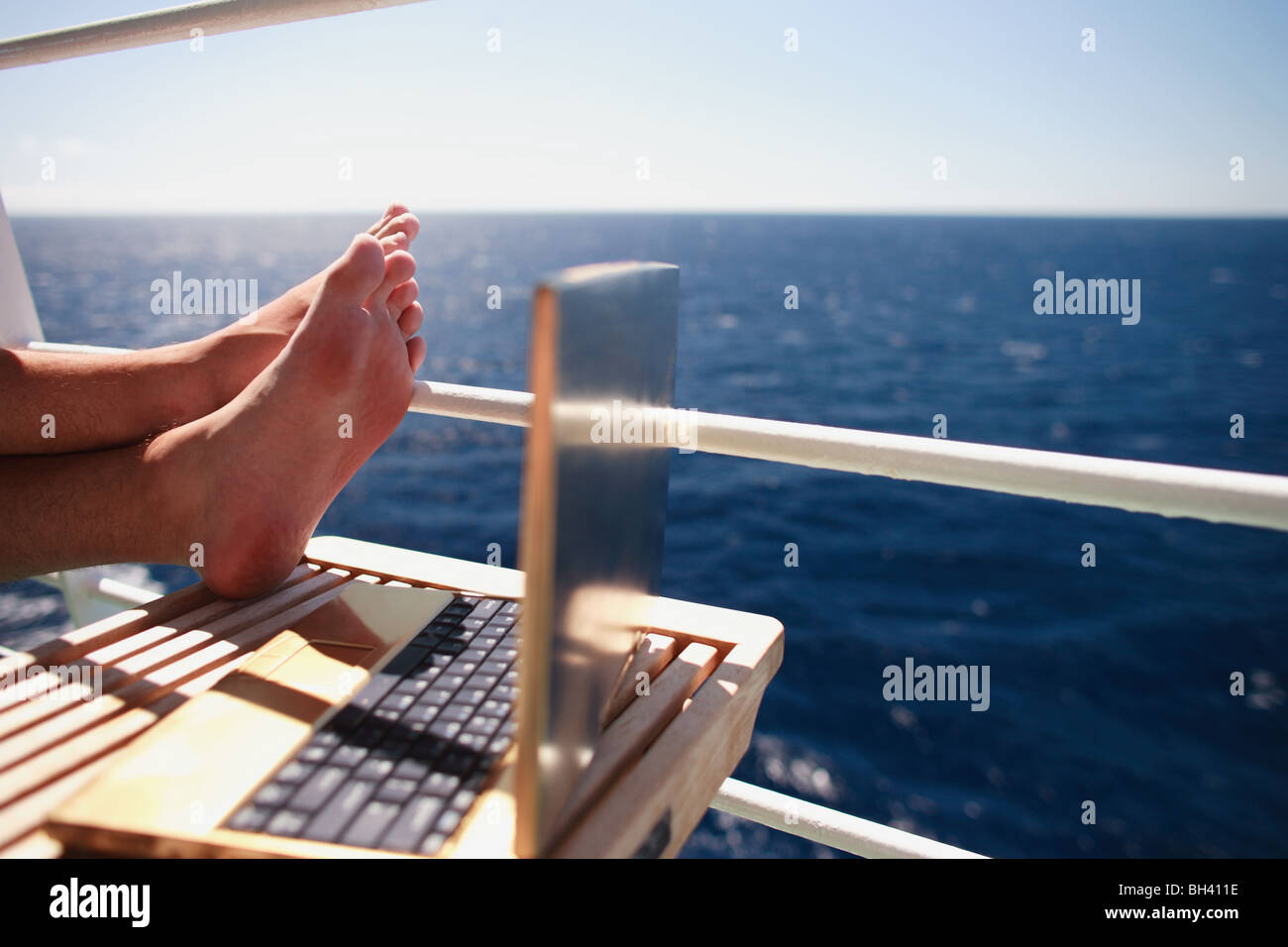 Ein Mann Füße entspannen neben einem Laptop-Computer, auf dem Balkon eines Kreuzfahrtschiffes Stockfoto