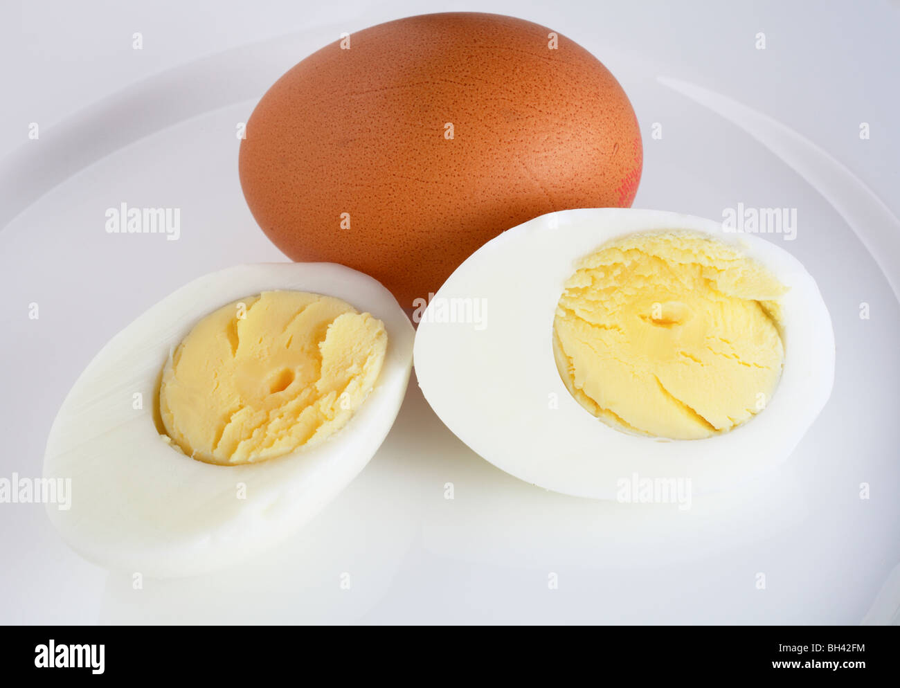 Nahaufnahme von einem in Scheiben geschnittenen gekochten Ei und ein frisches braune Ei auf einem weißen Teller Stockfoto