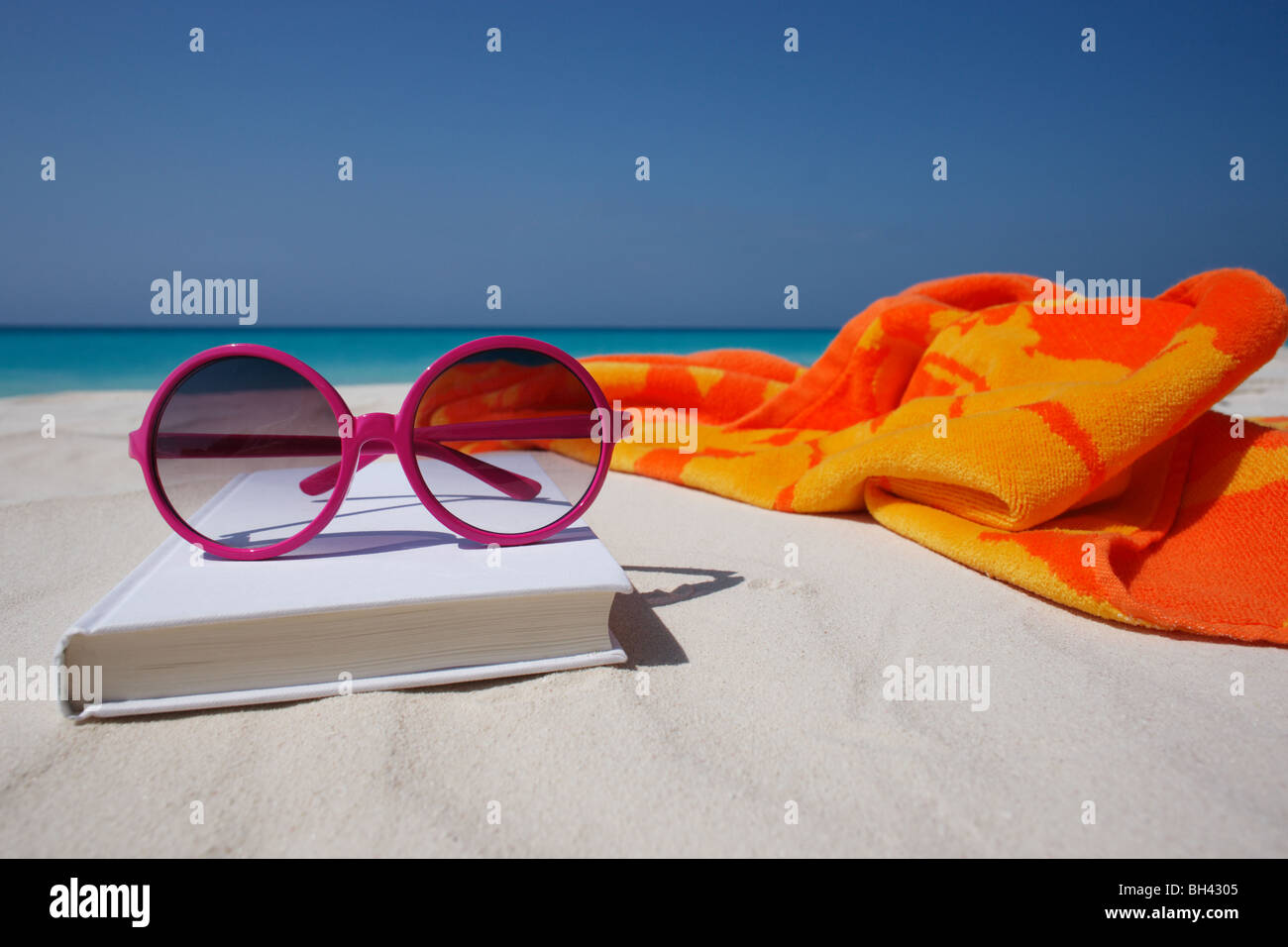 Rosa Sonnenbrille, Buch und Strand Handtuch auf einer menschenleeren Sandstrand Stockfoto