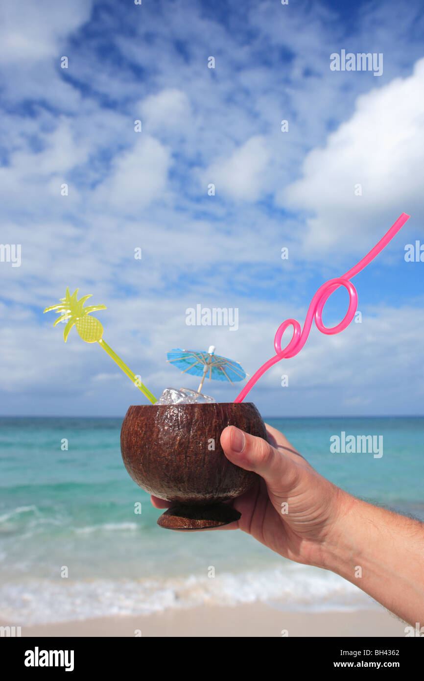 Eines Mannes Hand mit einem tropischen cocktail in einer Kokosnussschale auf einem einsamen tropischen Strand Stockfoto