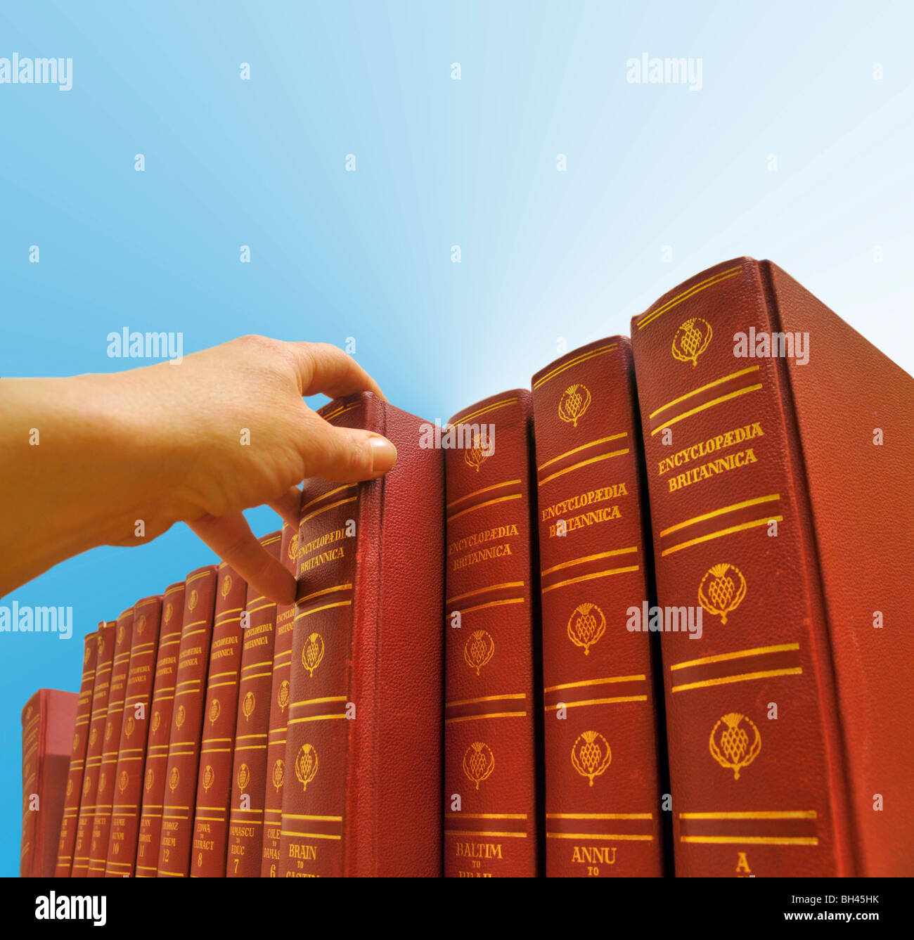Nahaufnahme der Hand einer Person, die eine Reihe von Enzyklopädie Britannica Bücher ein Volume auswählen. Stockfoto