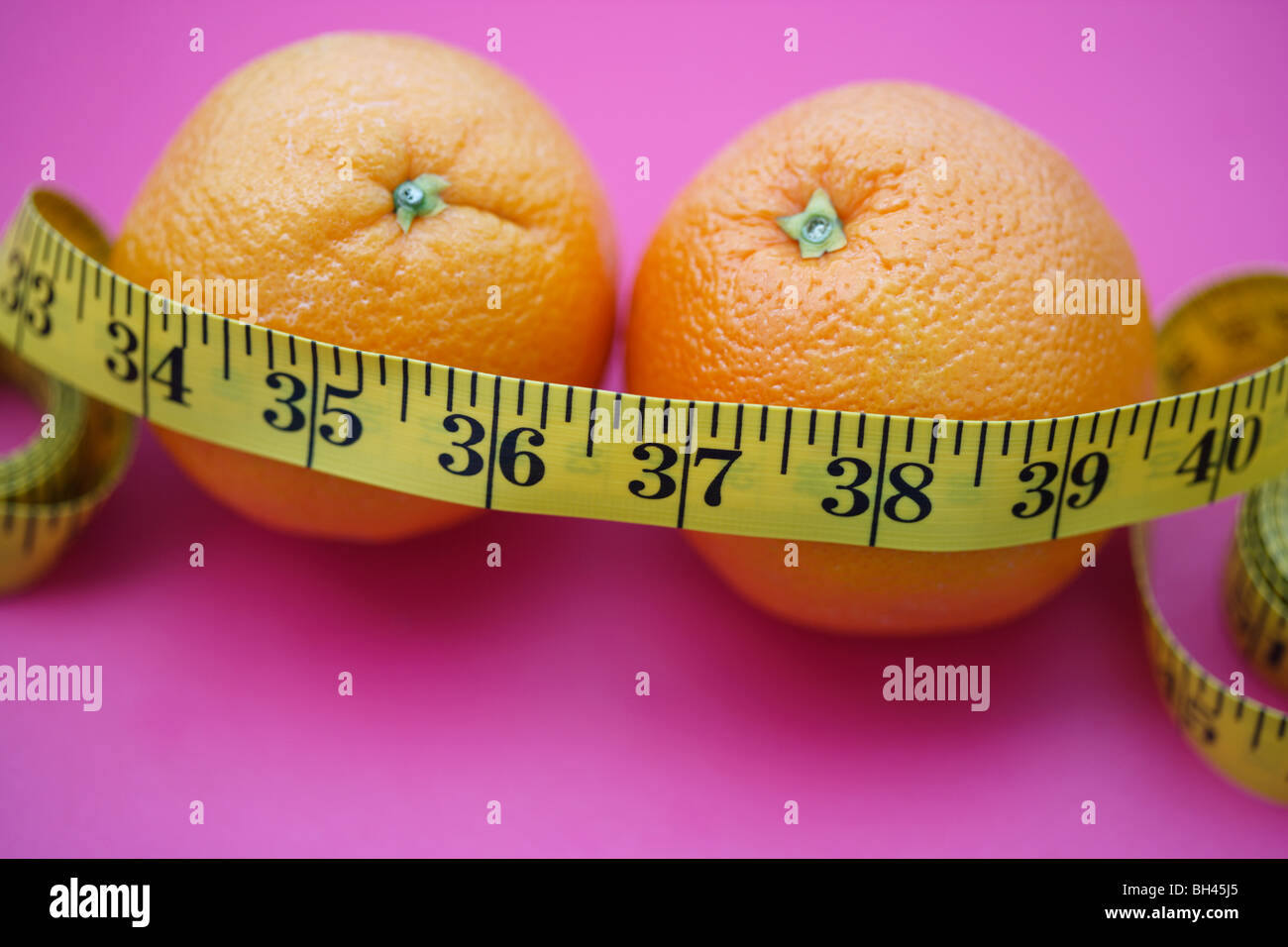 Ein Maßband, um ein paar Orangen auf lila Hintergrund gewickelt Stockfoto