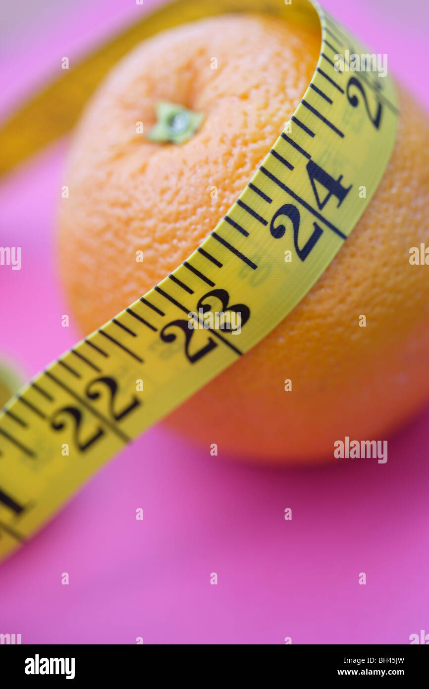 Ein Maßband, um eine Orange auf lila Hintergrund gewickelt Stockfoto