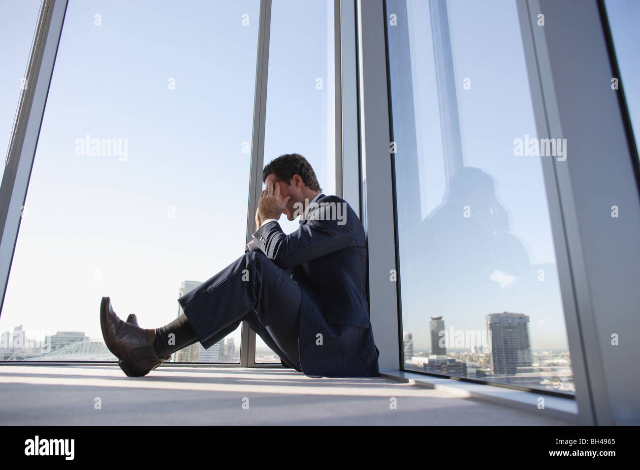 Ein Geschäftsmann, sitzen auf dem Boden in der Ecke ein Büro-Hochhaus mit seinen Kopf in seine Hände Stockfoto