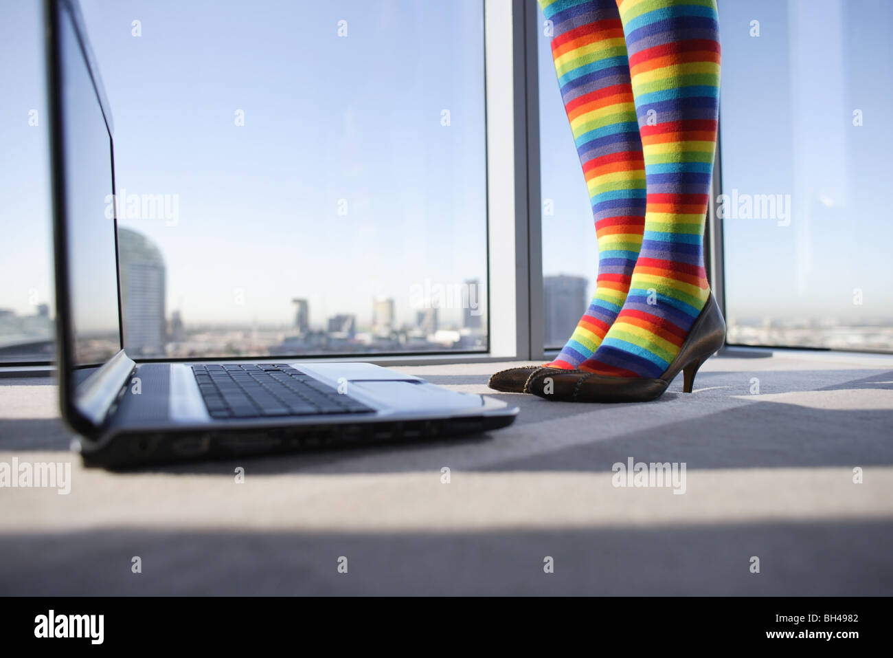 Eine Frau die Beine tragen Multi farbige gestreifte Strümpfe stehen neben einem Laptop-Computer in einem Büro Stockfoto