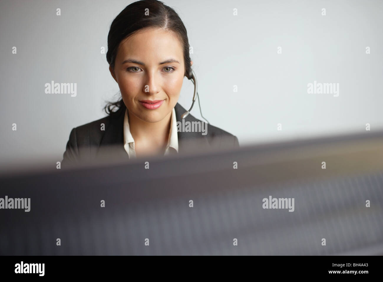 Junge Geschäftsfrau sitzen an einem Computer einen Kopfhörer tragen lächelnd Stockfoto