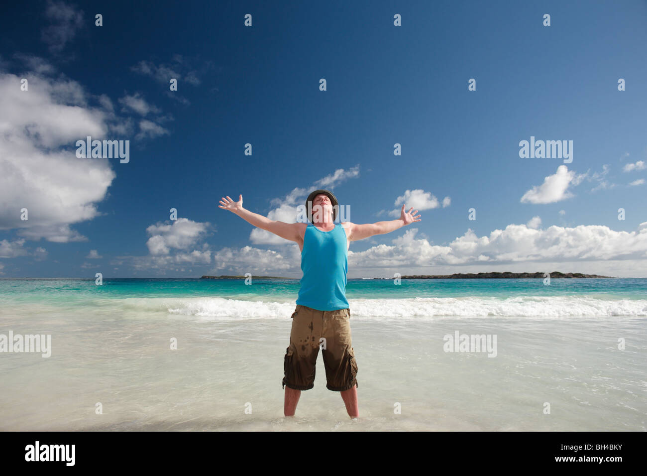 Junger Mann mit seiner Feier in den Himmel an einem tropischen Strand, erhobenen Armen lächelnd Stockfoto