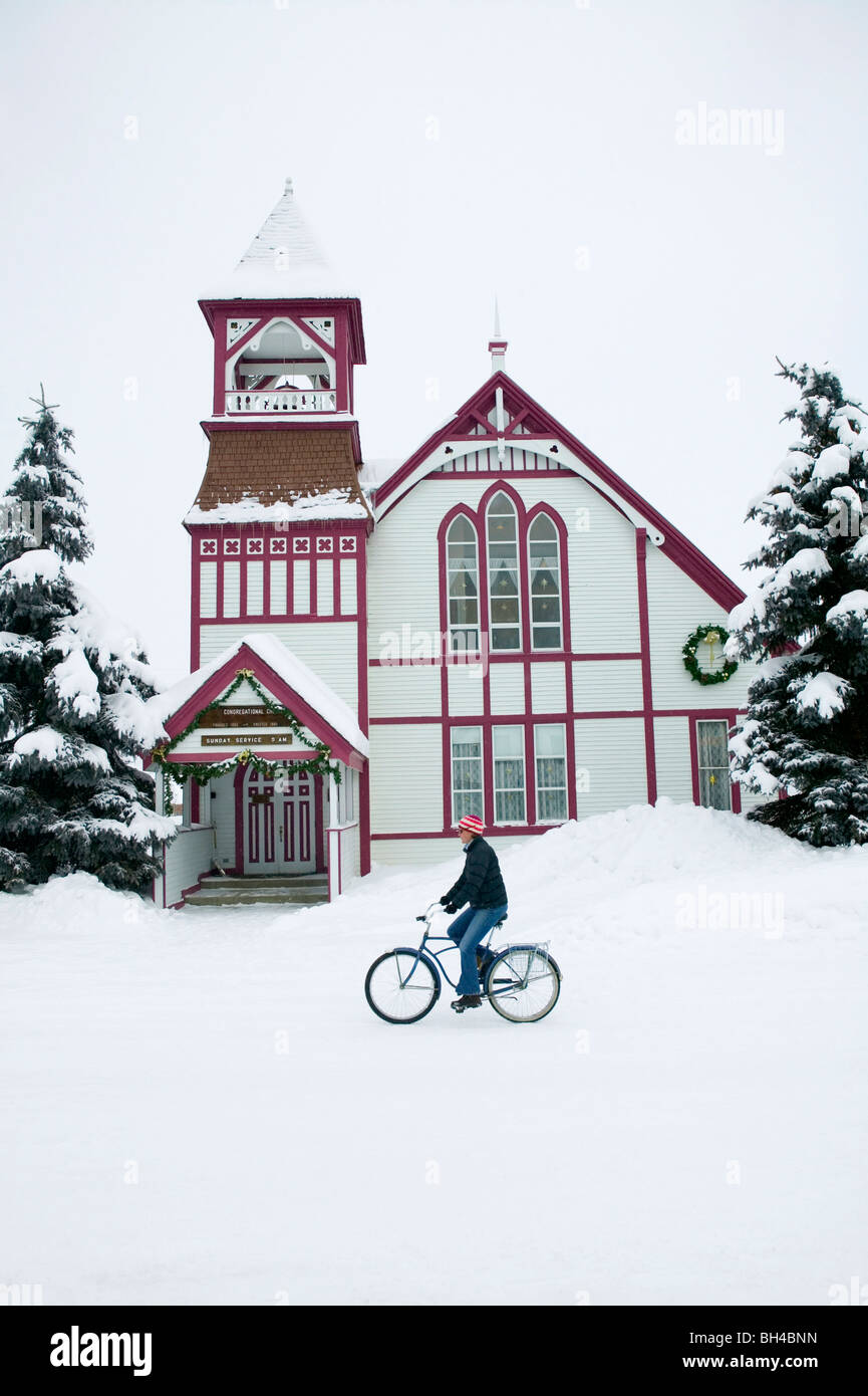 Frau mit dem Fahrrad auf einer Schnee bedeckten Straße vor einer Kirche, Crested Butte, Colorado. Stockfoto