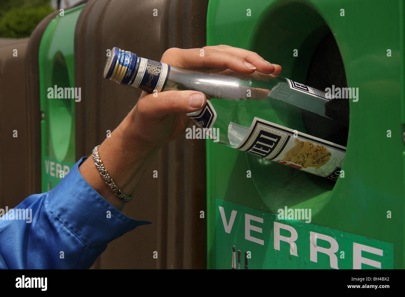 Nahaufnahme einer Hand setzen eine leere Flasche in einen Recycling-Behälter. Stockfoto