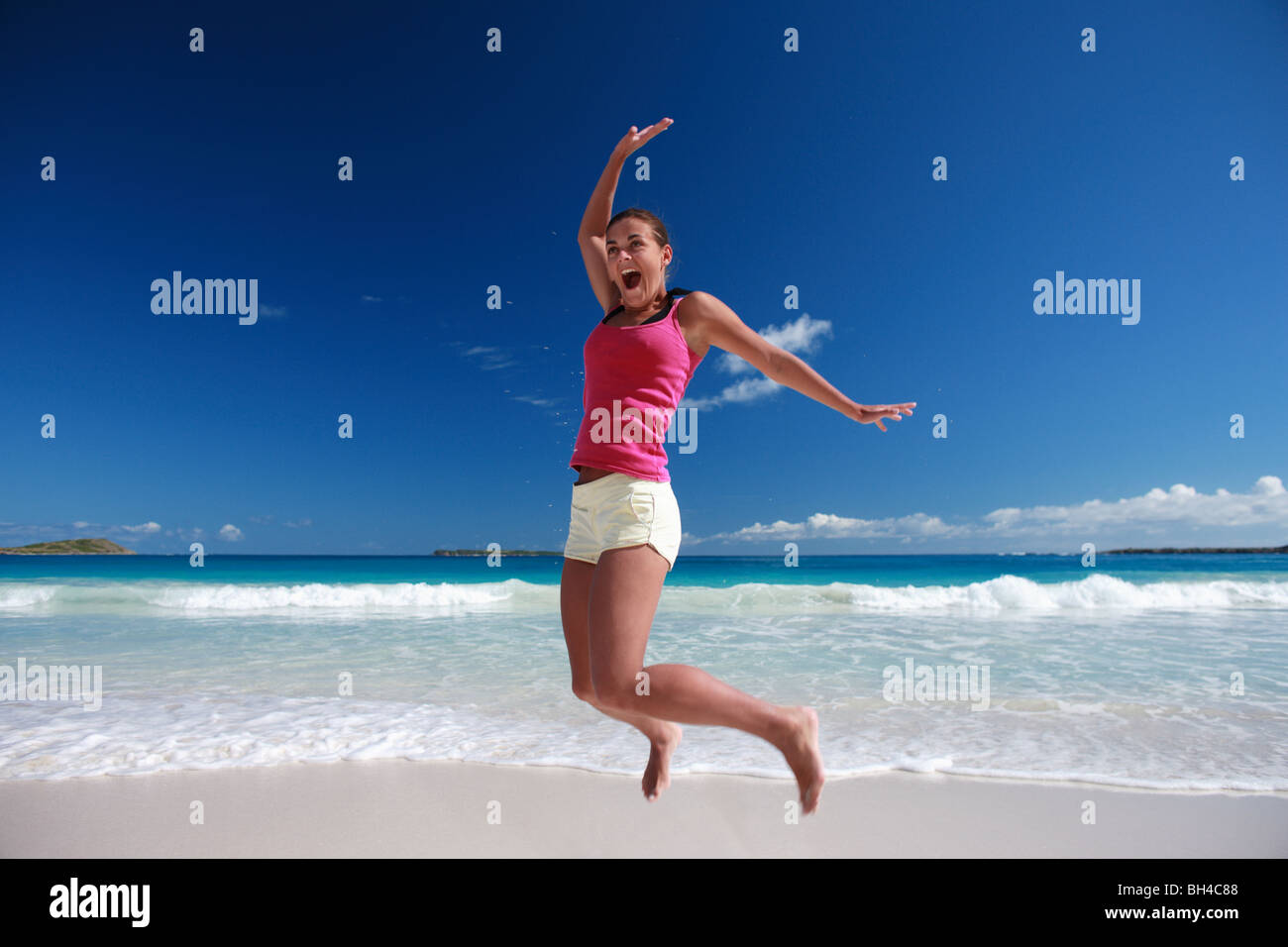 Junge Frau in die Luft springen, auf einem einsamen tropischen Strand lächelnd Stockfoto