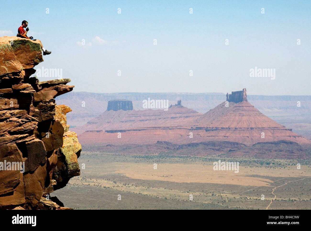 Ein junger Mann sitzt auf einem Felsen während des Essens einer oranges auf der Porcupine Rim Trail in Moab, Utah. Stockfoto