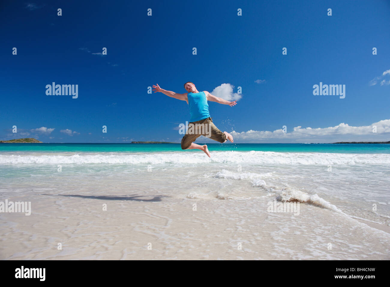 Junger Mann springt in die Luft auf einem einsamen tropischen Strand, Lächeln Stockfoto