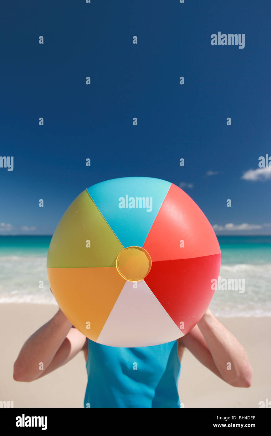 Junger Mann hält einen aufblasbaren Wasserball über sein Gesicht auf einem einsamen tropischen Strand Stockfoto