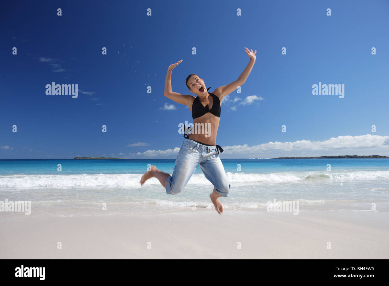 Junge Frau in die Luft springen, auf einem einsamen tropischen Strand lächelnd Stockfoto