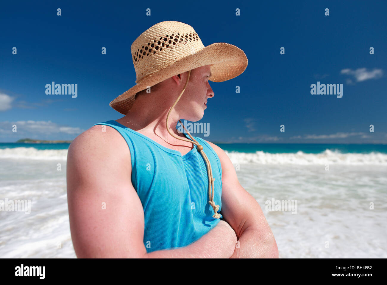Junge Mann trägt einen Strohhut mit Blick auf das Meer an einem tropischen Strand Stockfoto