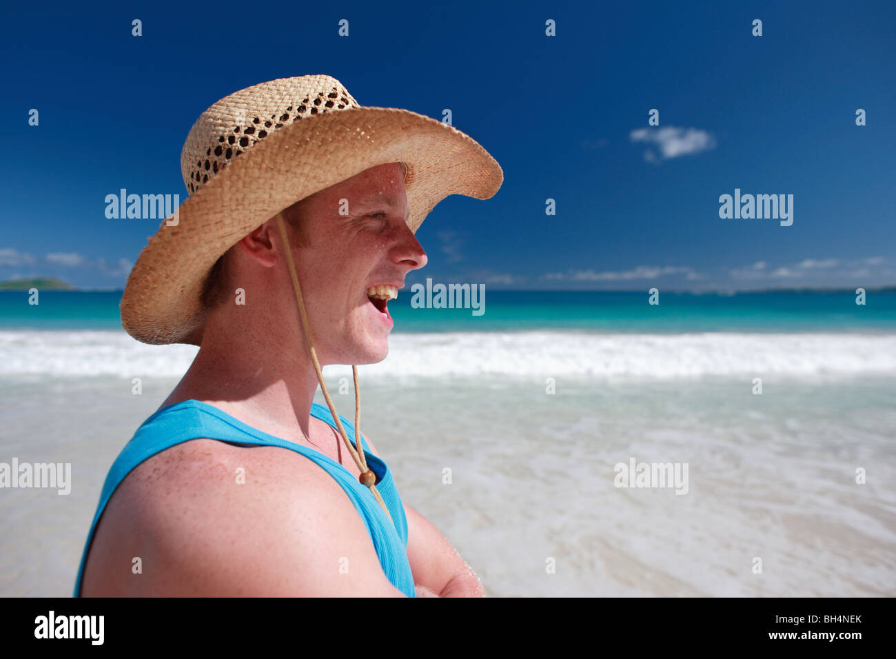 Junge Mann trägt einen Strohhut mit Blick auf das Meer an einem tropischen Strand, lachen Stockfoto