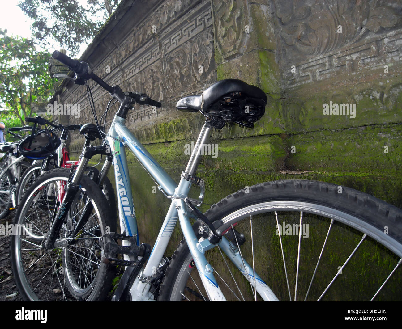 Fahrräder geparkt gegen alte geschnitzte moosigen Steinmauer während der Radtour, Bali, Indonesien. Keine PR Stockfoto
