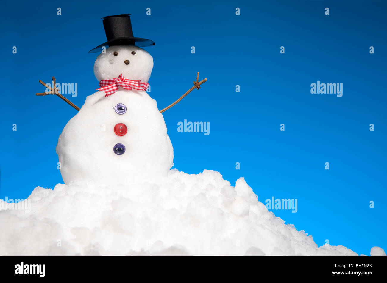 Miniatur-Schneemann auf Schnee mit blauem Himmel hinter Stockfoto