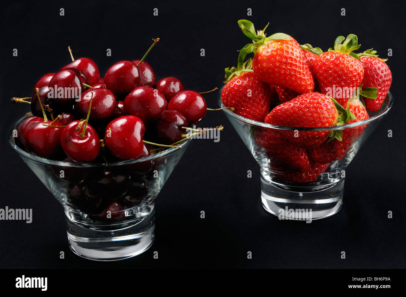 Glasschalen von Kirschen und Erdbeeren auf schwarz Stockfoto