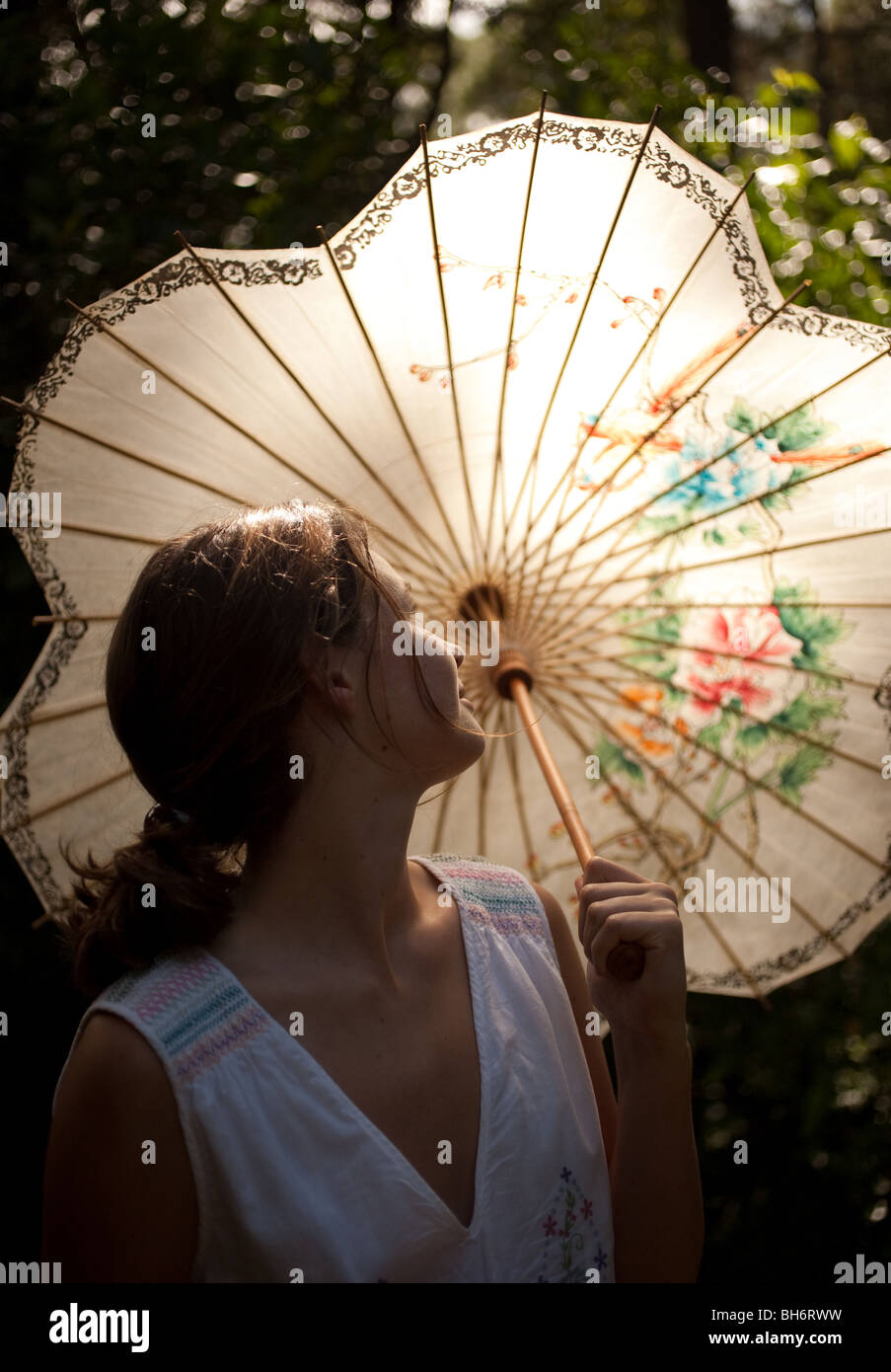 Ein junges Mädchen steht in ihrem Garten unter ihrem chinesischen Schirm. Stockfoto