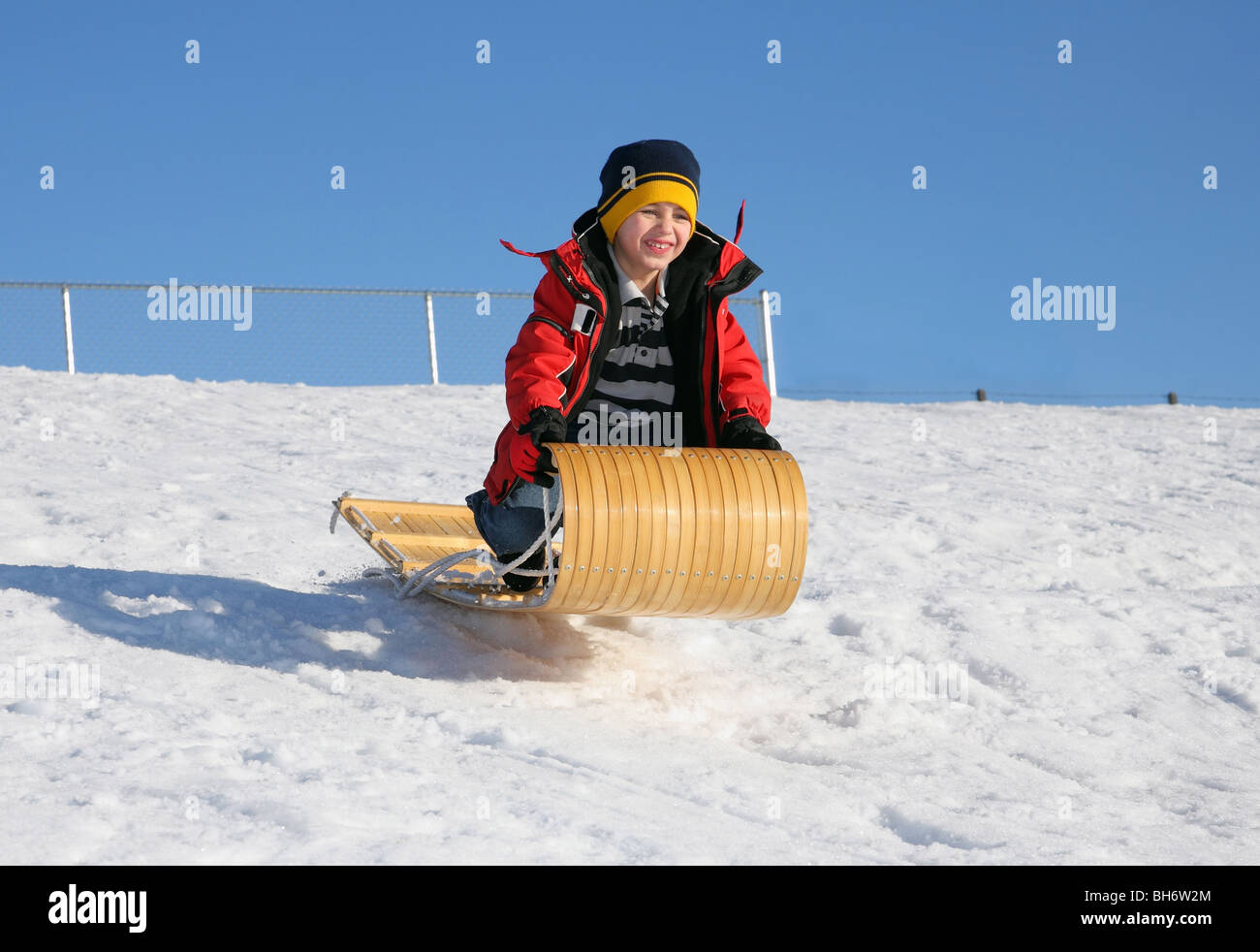 kleiner Junge mit einem Holz Rodel geht aus einem verschneiten Sprung Stockfoto