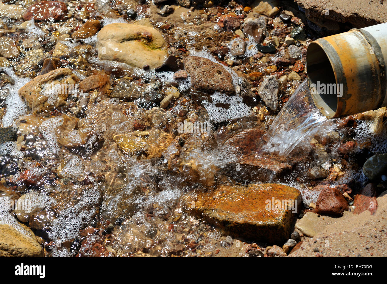 Wasser fließt aus Rohr auf Kieselsteine am Strand Stockfoto