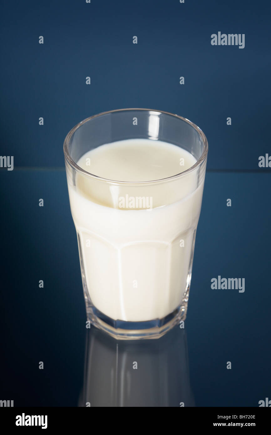 Milch in ein Glas auf blauem Hintergrund reflektiert Stockfoto