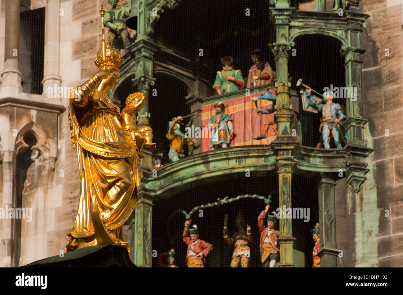 Goldene Statue der Jungfrau Maria schimmert in der Sonne neben berühmten Glockenspiel Rathaus München Stockfoto