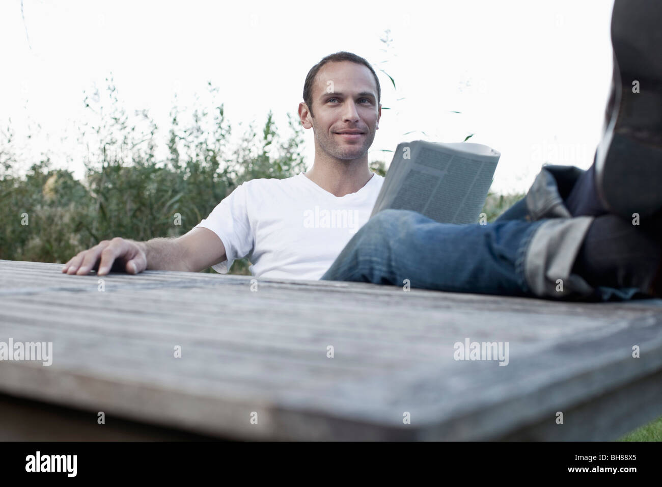 Ein Mann sitzt an einem freien Tisch Lesen einer Zeitschrift, nicht-städtisches Motiv Stockfoto