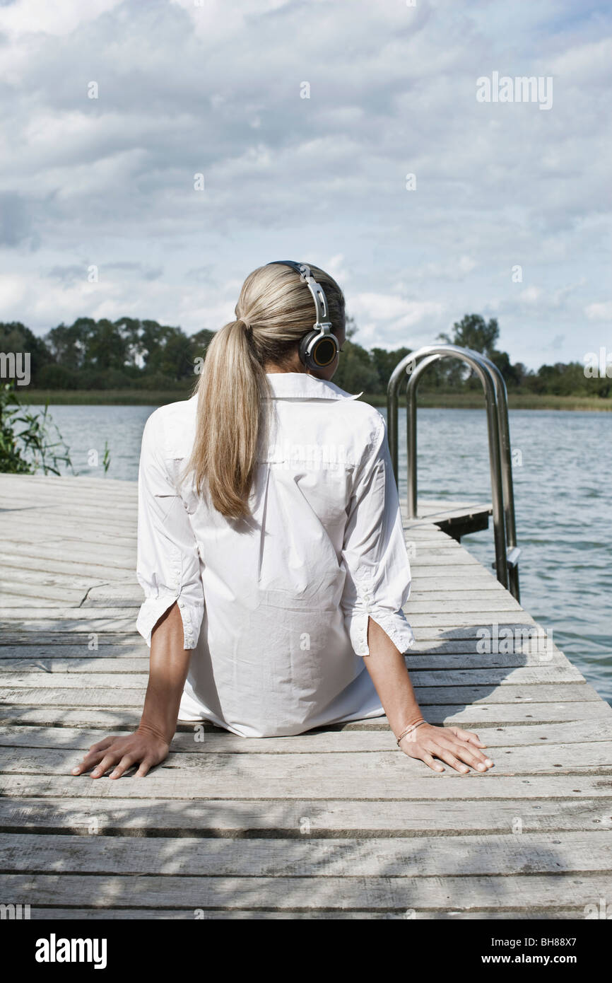 Eine Frau trägt Kopfhörer entspannend auf einem Steg Stockfoto
