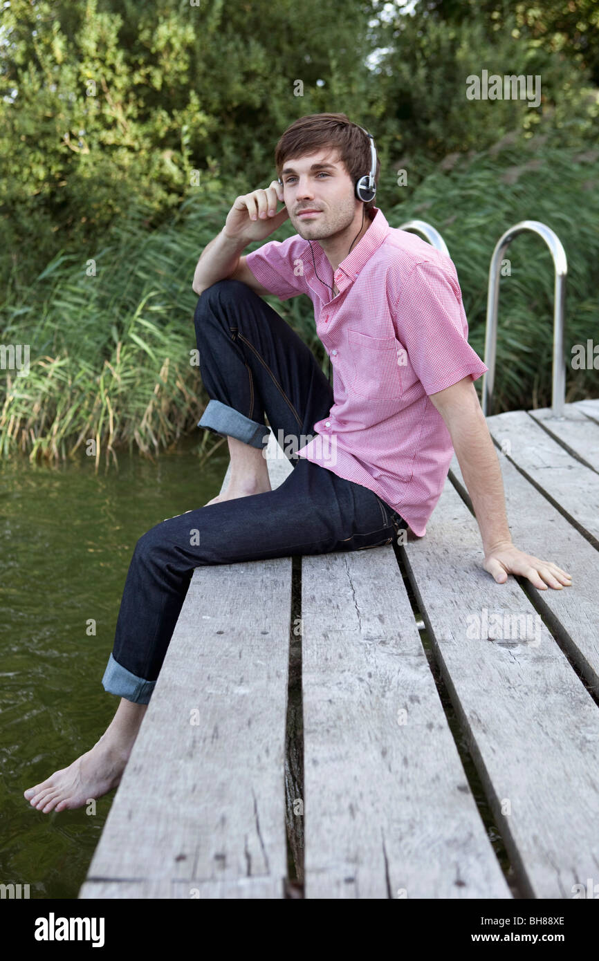 Ein Mann mit Kopfhörern entspannend auf einem Steg Stockfoto