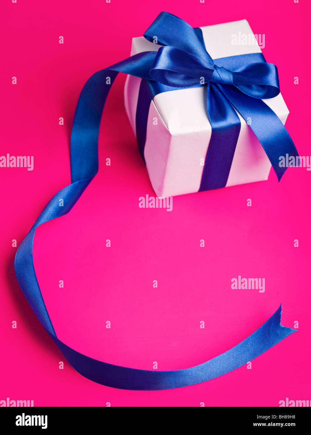 weiße Geschenk in ein blaues Band auf einem rosa Hintergrund Stockfoto