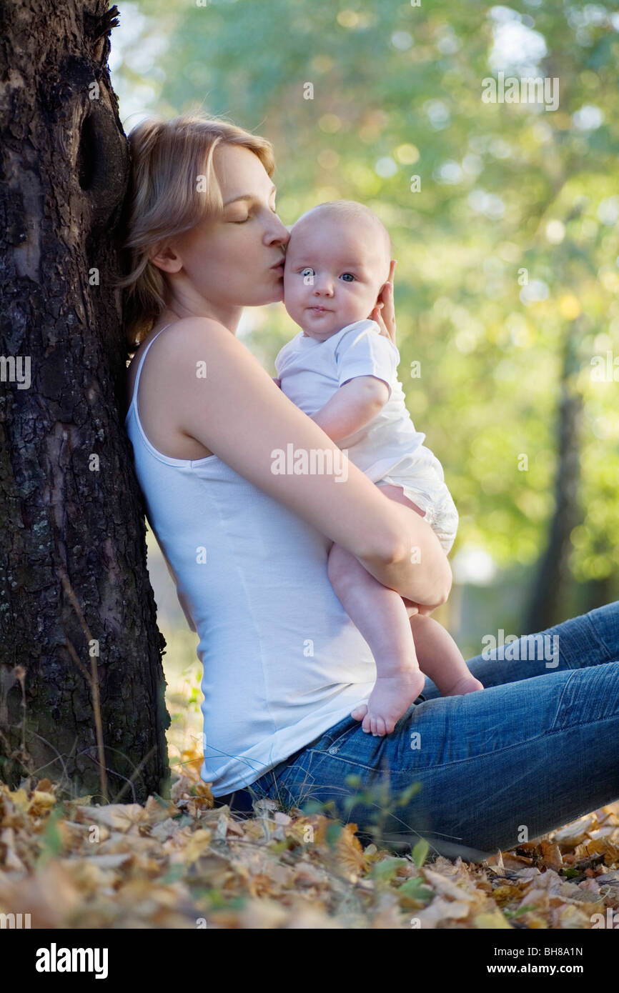 Eine Mutter gegen einen Baum, küssen ihr Baby sitzen Stockfoto