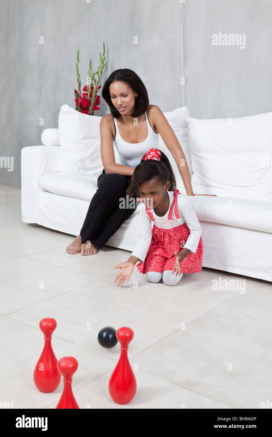 Ein junges Mädchen spielen mit einem Spielzeug bowling Set während ihrer Mutter-Uhren Stockfoto