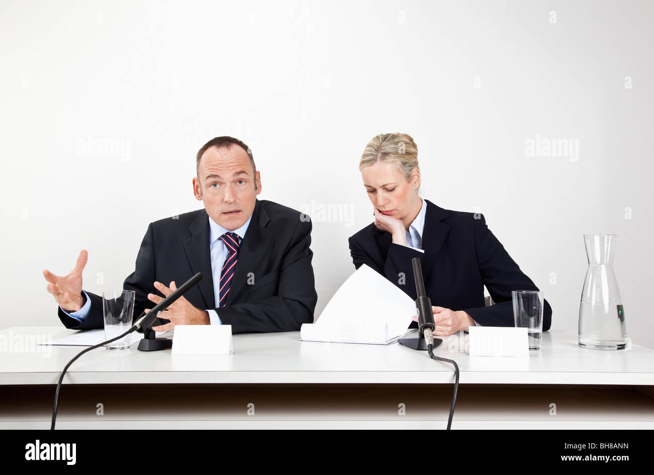 Ein Mann und eine Frau sitzen an einem Schreibtisch mit Mikrofonen und Dokumente Stockfoto