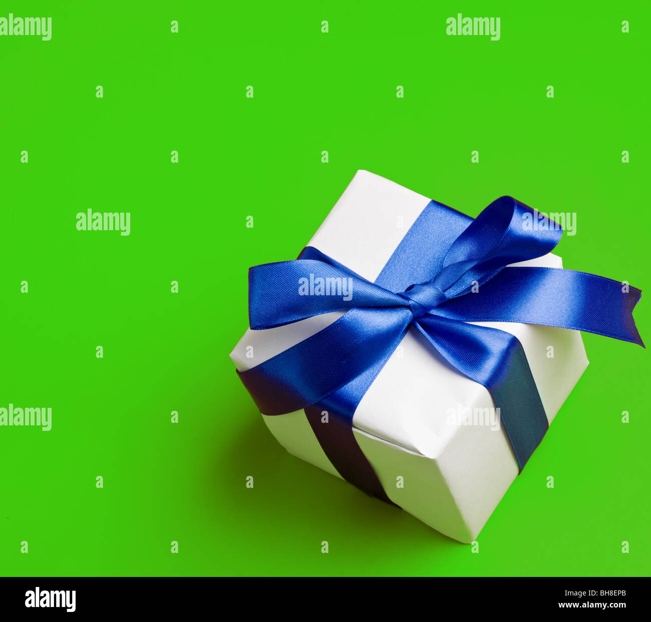 weiße Geschenk in ein blaues Band auf grünem Hintergrund Stockfoto