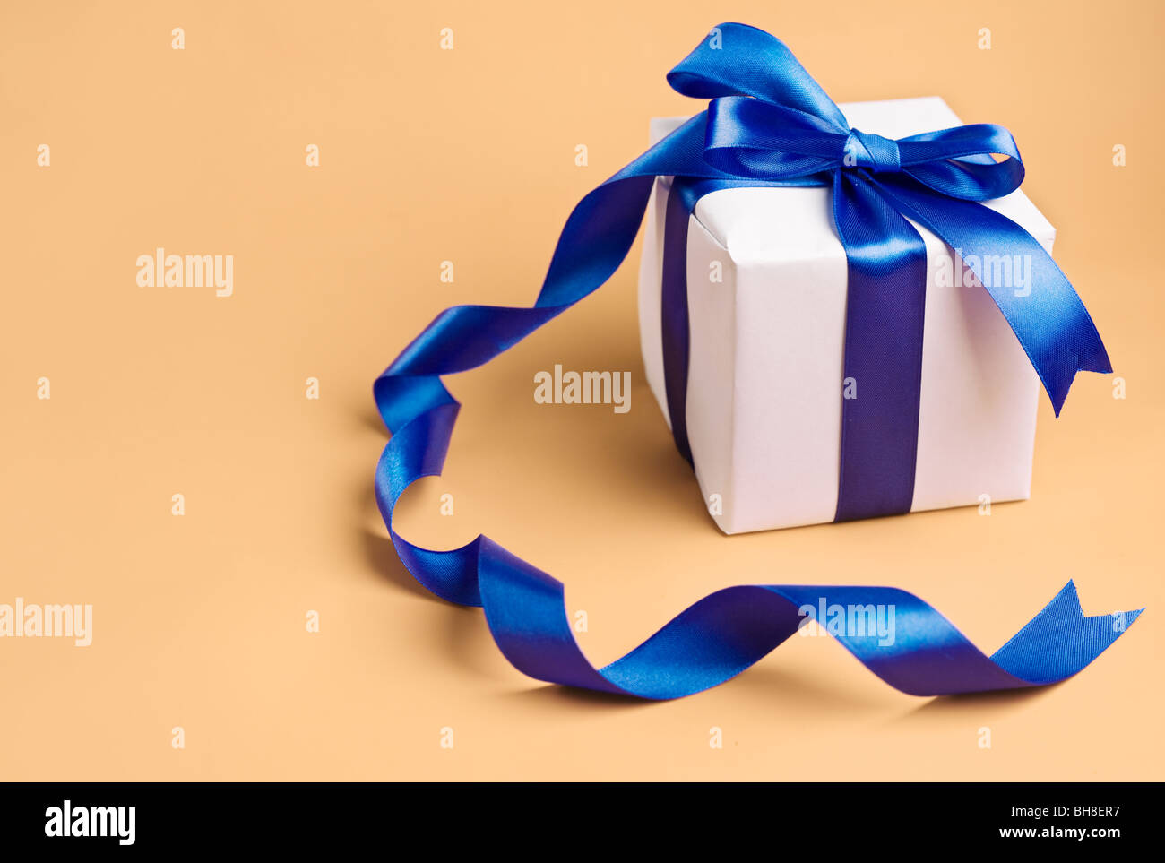 weiße Geschenk mit blauem Band auf einem Biege-Hintergrund Stockfoto