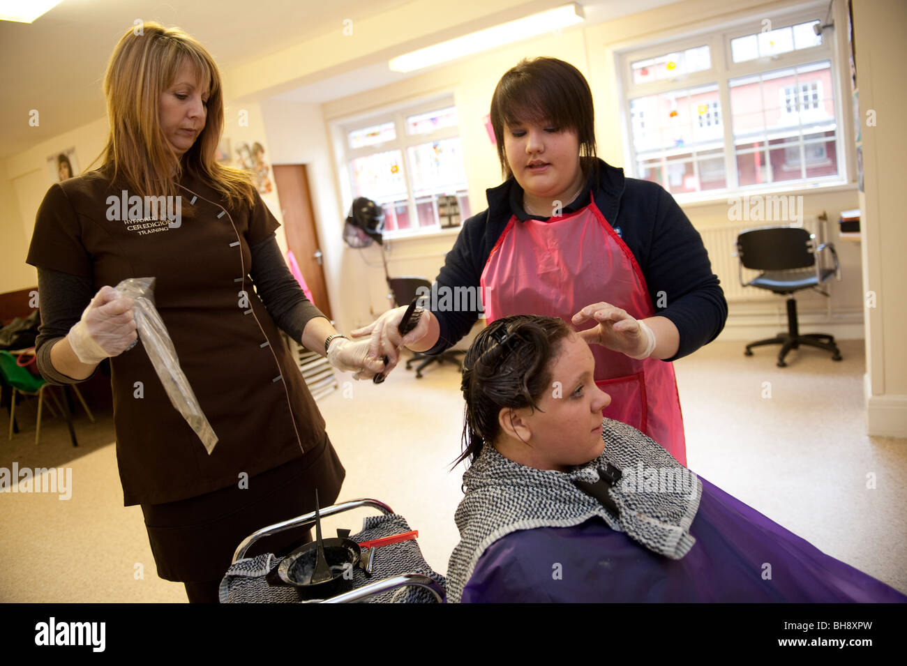 Eine Frau berufliche Tutor Lehre Friseur Fähigkeiten zu zwei Mädchen im Teenageralter in der Sekundarschule, UK Stockfoto