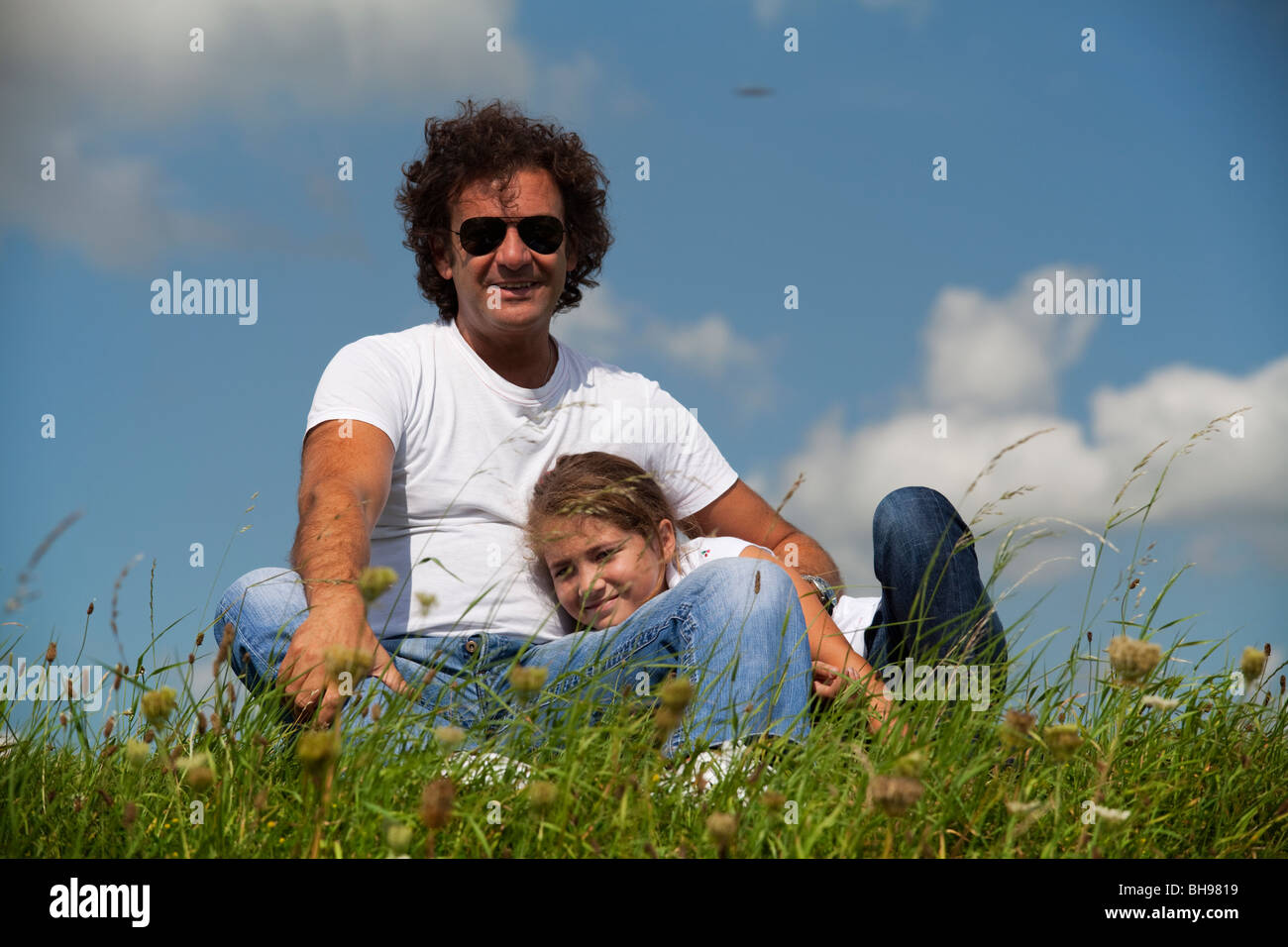 Vater und Tochter im Grünen mit blauen Himmel und flauschigen Wolken als Hintergrund Stockfoto