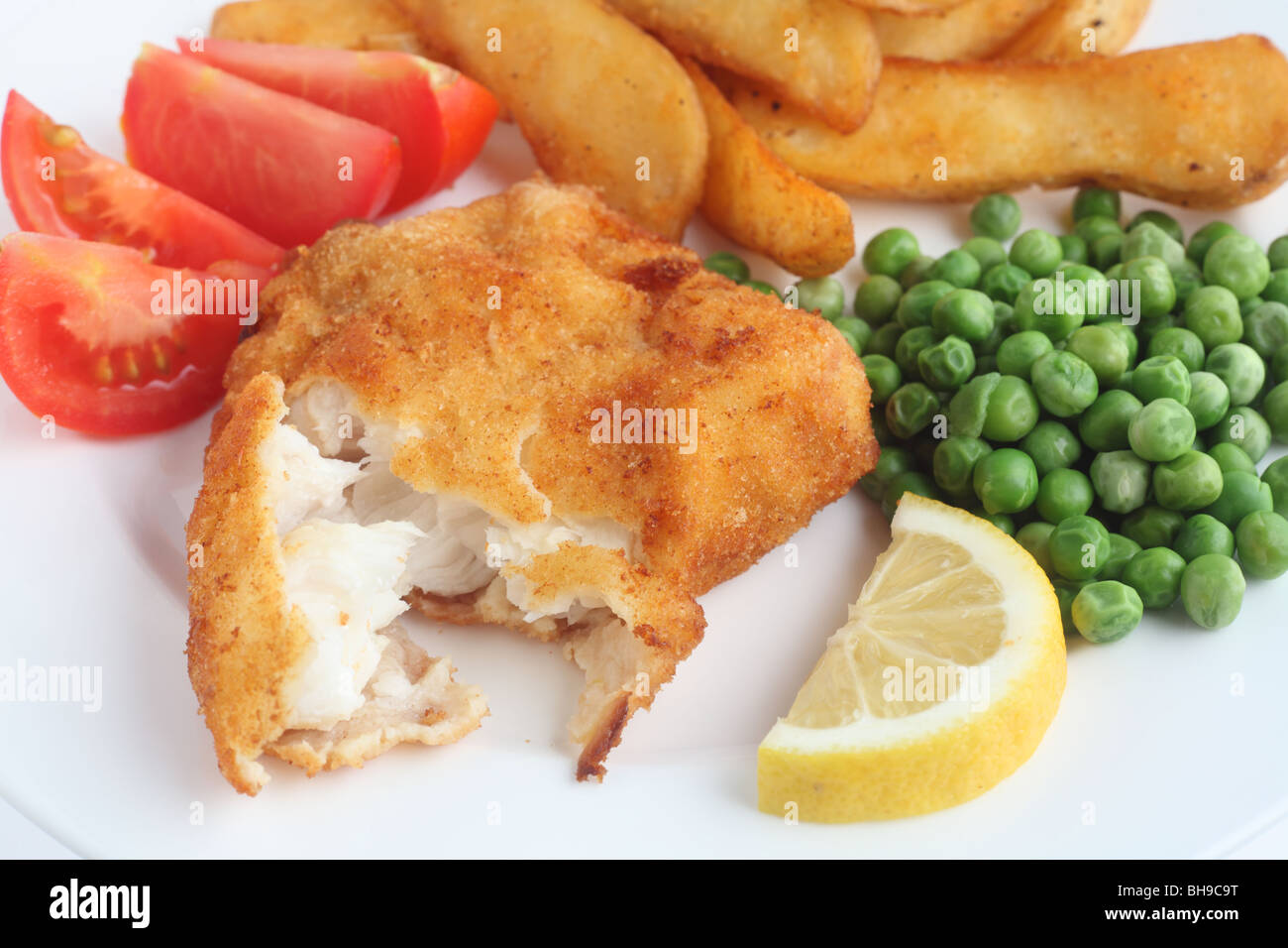 Eine Mahlzeit aus einem panierte weißen Fischfilet mit klobigen gebratene Kartoffelspalten, Erbsen, Tomaten und Zitrone Stockfoto
