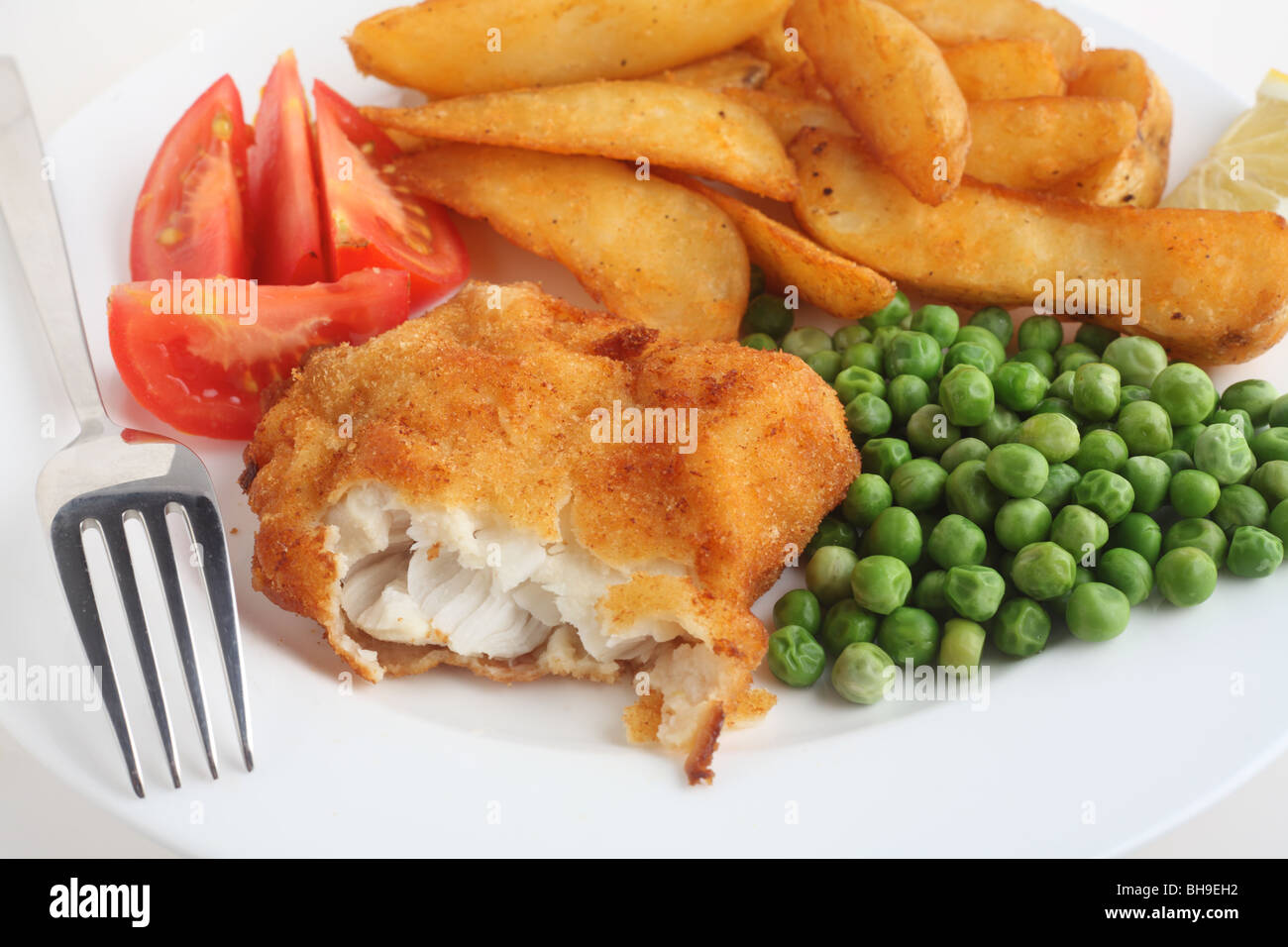 Panierte Hamour weißen Fisch, mit Kartoffelspalten, Erbsen, Zitronensaft und in Scheiben geschnittenen Tomaten und einer Gabel Stockfoto