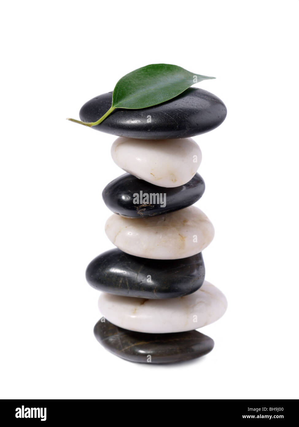 Black And White Stones gestapelt mit grünen Blatt an der Spitze auf weißem Hintergrund Stockfoto